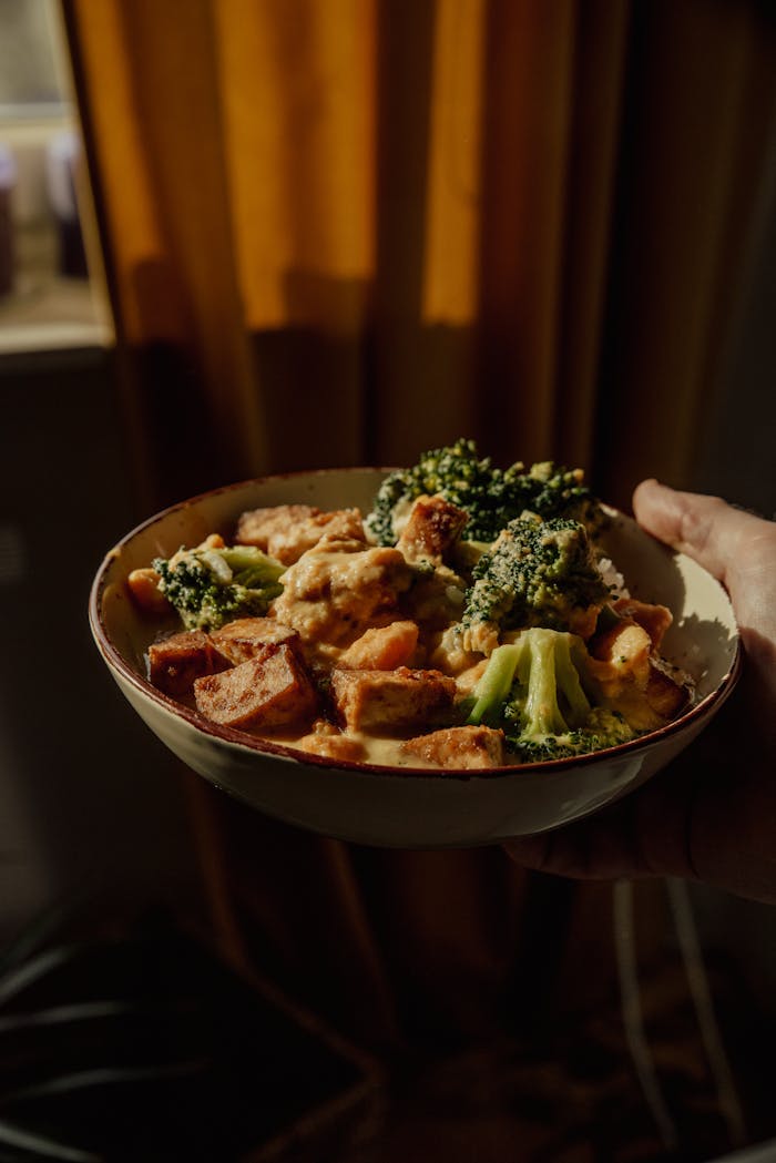 A delicious bowl of broccoli and tofu, captured in warm indoor lighting, perfect for a cozy meal setting.